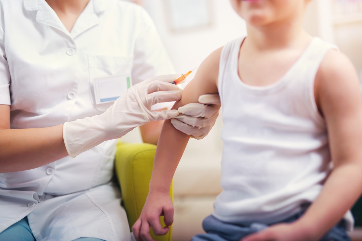 Impfung eines Kindes - der Arzt impft das Kind - das Kind sitzt und der Arzt gibt ihm eine Spritze in den Arm.