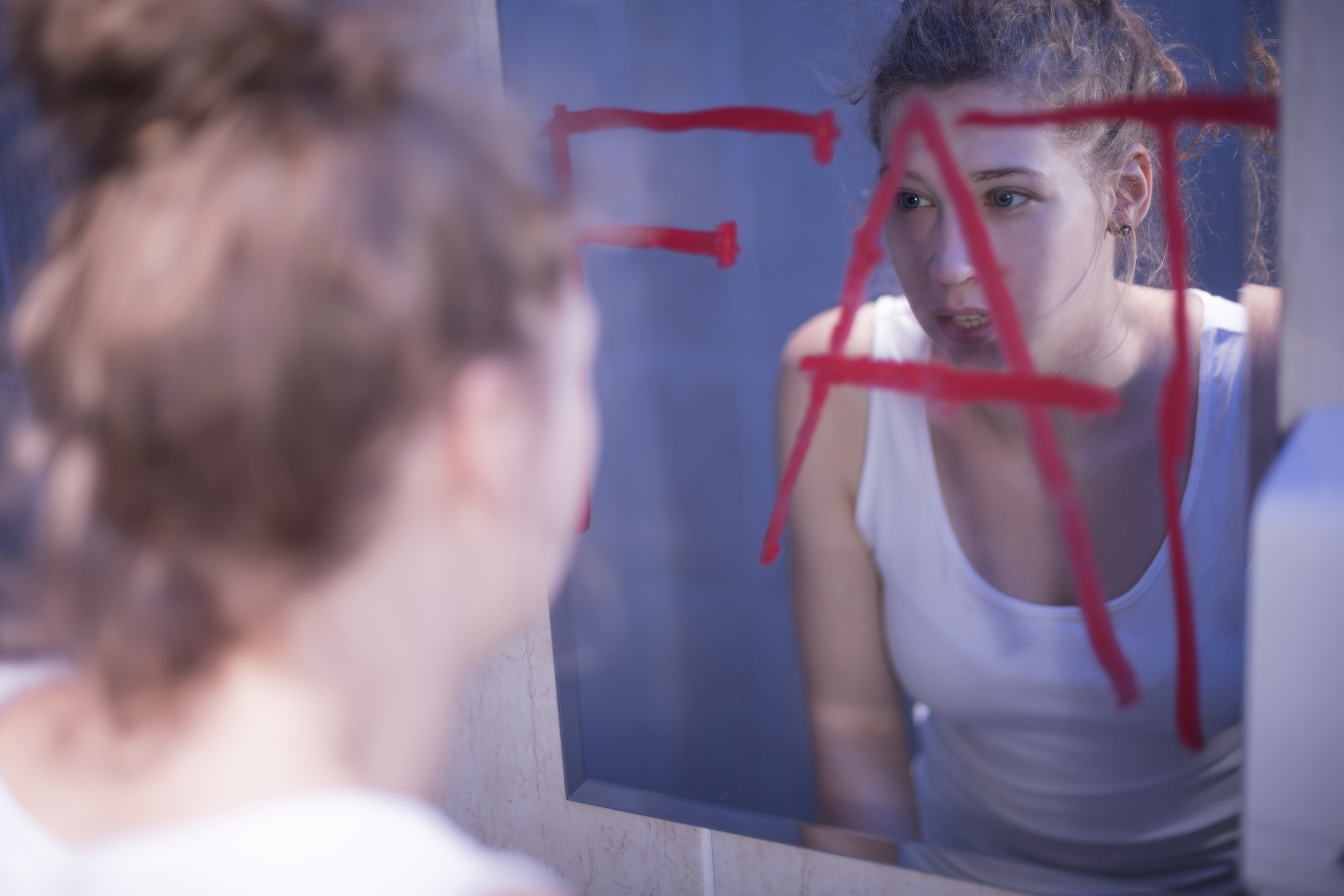 Eine junge Frau, die sich beim Blick in den Spiegel für fett hält.