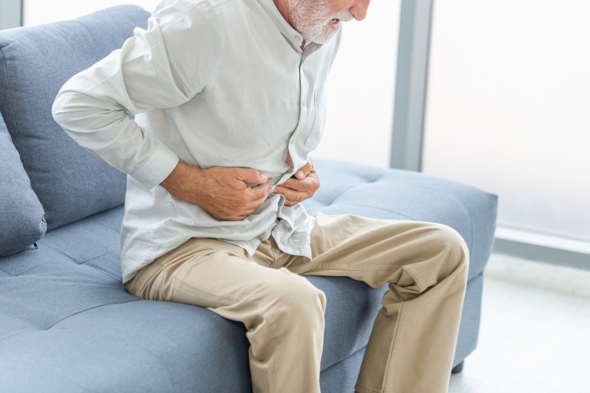 Ein älterer Mensch hat Unterleibsschmerzen - er sitzt in Bauchlage und hält sich den Bauch mit den Händen.