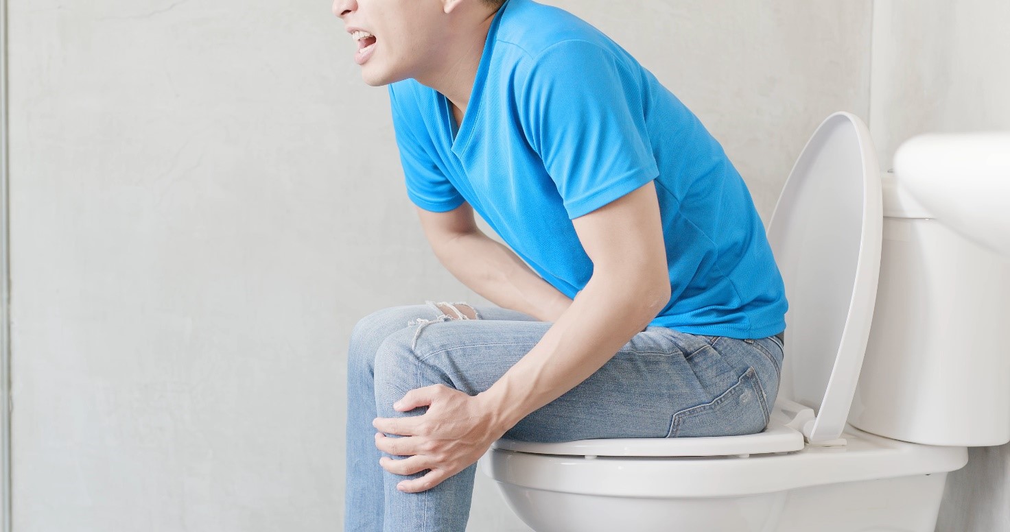 Die Person sitzt auf der Toilette und hat Unterleibsschmerzen.