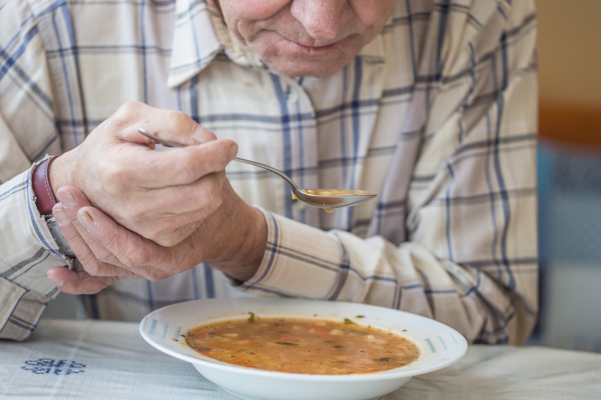 Mann isst Suppe und hält seine Hand gegen das Zittern bei Parkinson-Krankheit