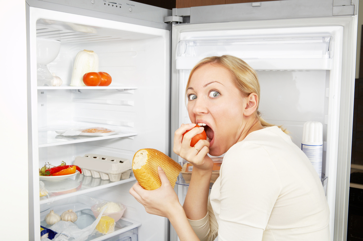 Eine Frau im Kühlschrank als Zeichen von übermäßigem Essen bei Bulimie