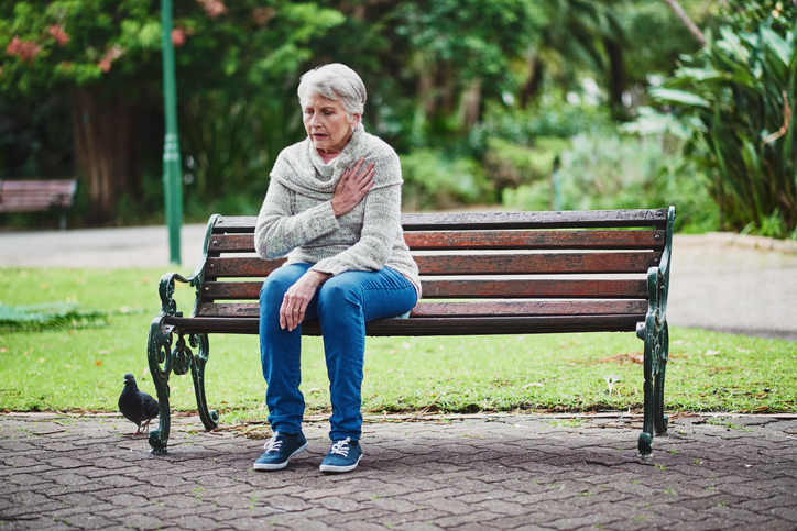 Eine ältere Frau sitzt auf einer Bank und hat Herzprobleme.