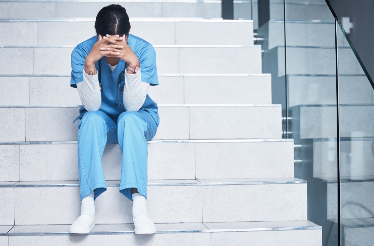 Eine Krankenschwester sitzt erschöpft auf der Treppe und leidet unter dem Burnout-Syndrom