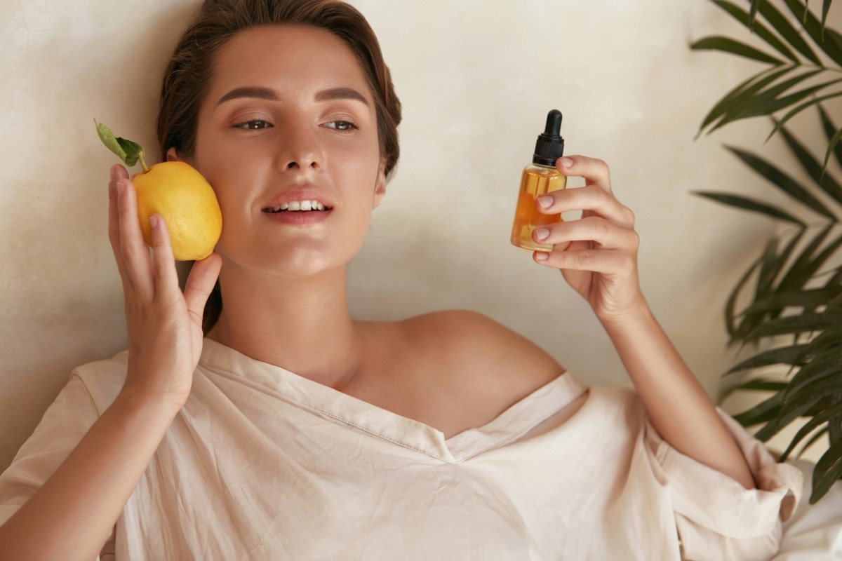 Frau mit einer Zitrone und einer Flasche mit Vitamin-C-Extrakt in der Hand, einem Vitamin, das der Haut hilft