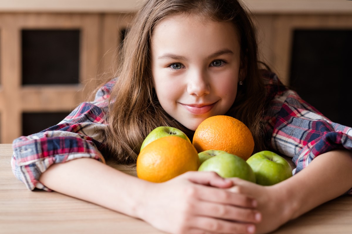 Vitamin C, in Früchten, ein Kind hält Orangen und Äpfel in den Armen