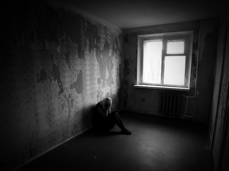 eine Frau, die in einem dunklen Raum sitzt, an die Wand gelehnt und ihr Gesicht mit den Händen festhält