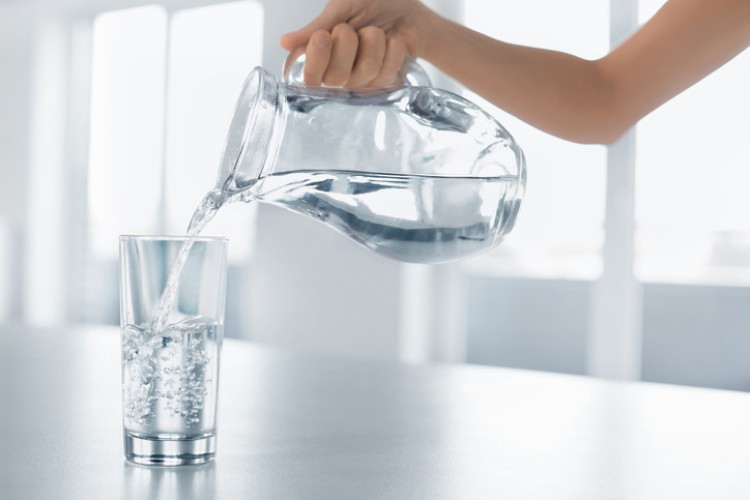 eine Hand, die sauberes Wasser aus einer Flasche in ein Glas gießt