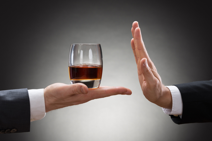 die Hand einer Person hält ein Glas Alkohol und die Hand einer anderen Person lehnt es ab
