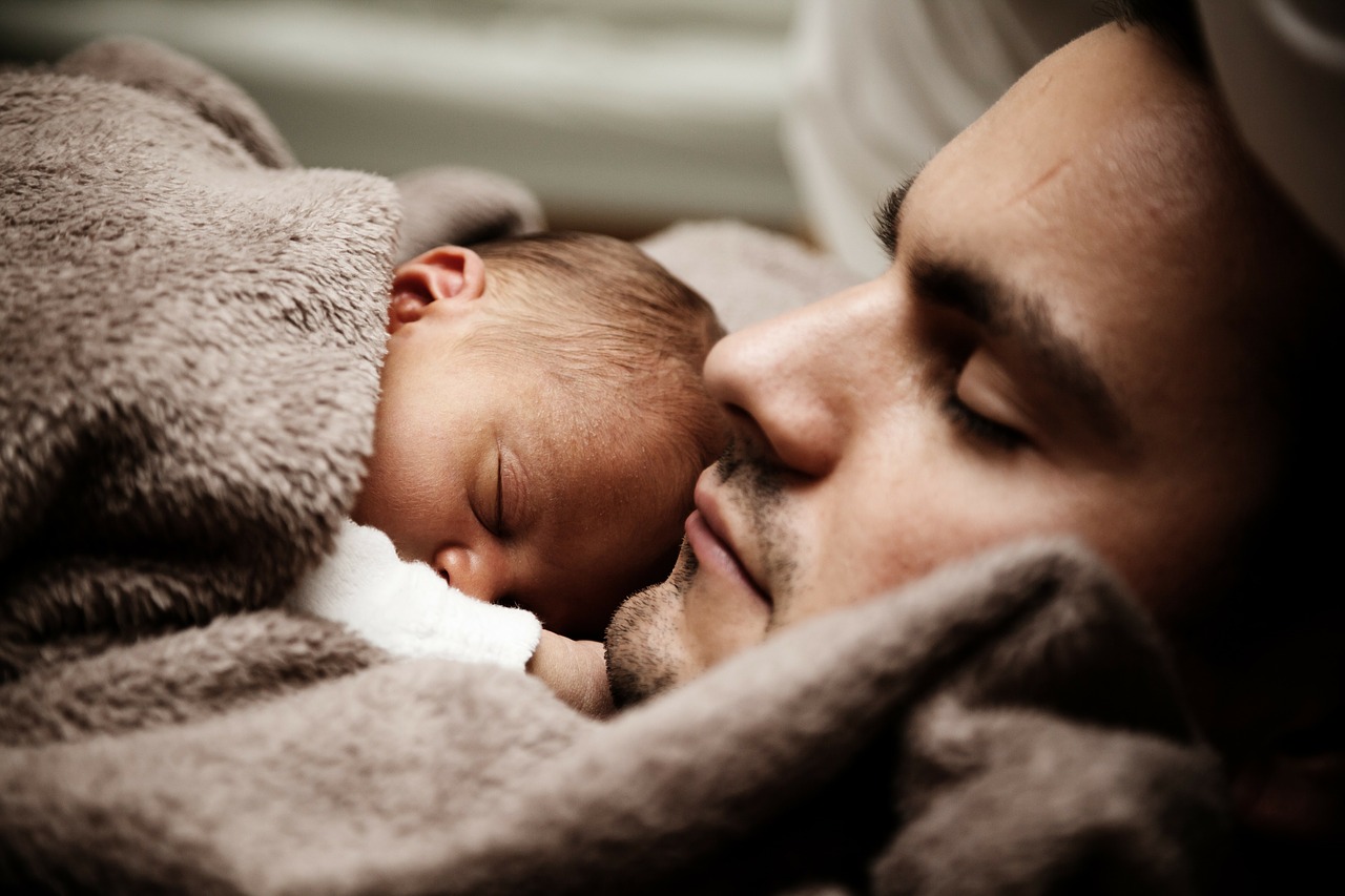 das Baby schläft neben seinem Vater unter einer braunen Decke