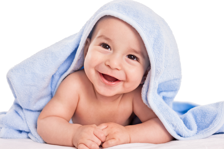 ein lachendes Baby auf dem Bauch, zugedeckt mit einem Handtuch