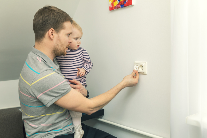 Papa hält ein kleines Kind im Arm und schließt den Stecker mit einem Elektrostecker