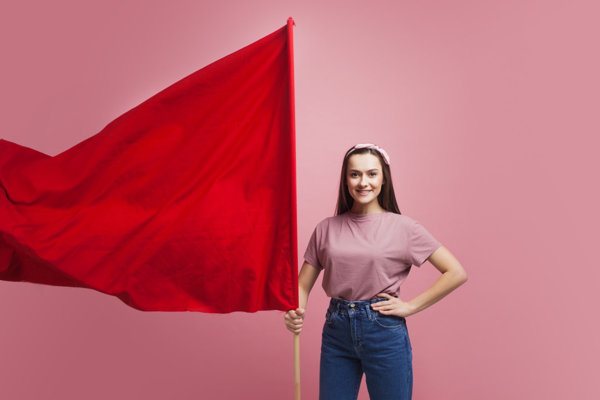 Eine Frau hält eine große rote Fahne als Warnung in der Hand.