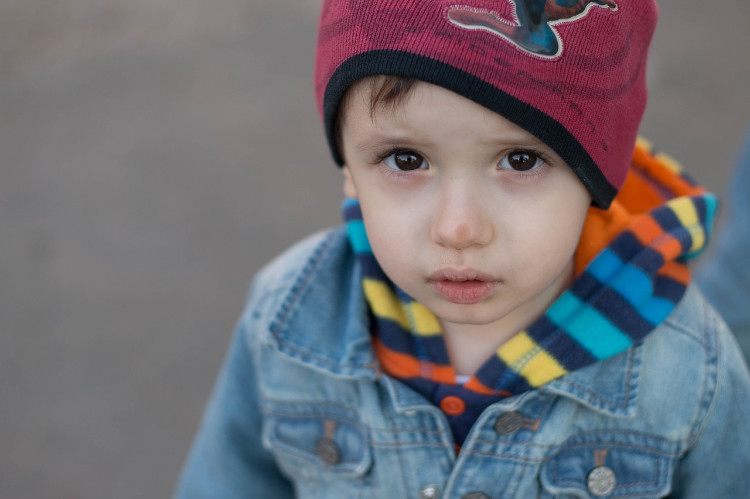 ein Kind mit blauer Jacke und roter Mütze schaut in die Linse