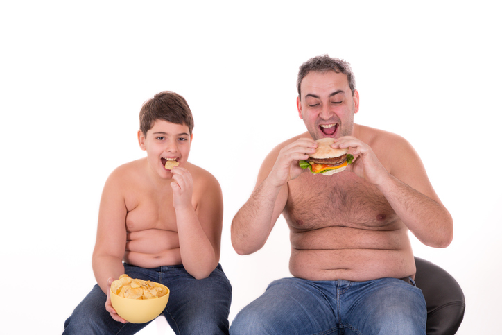 der Junge und sein Vater essen das falsche Essen, essen Hamburger, sind fettleibig