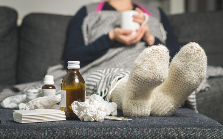 eine kranke Frau liegt im Bett mit warmen Socken und Tabletten und Sirup neben ihr