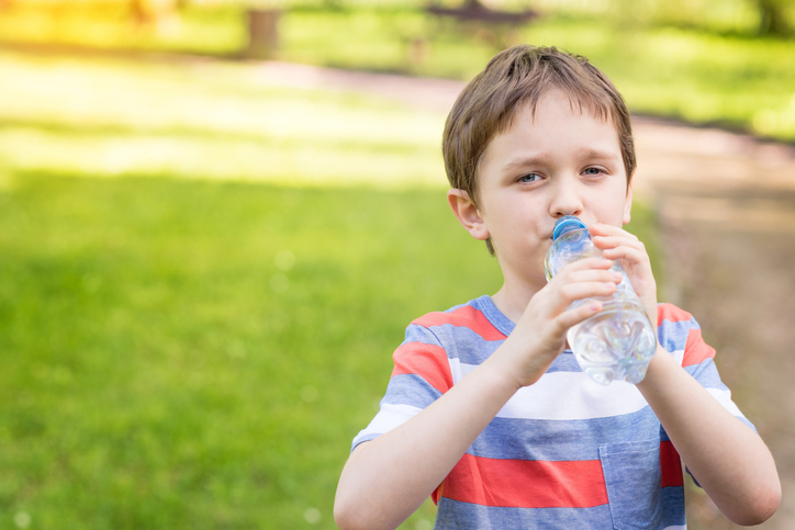 Junge trinkt Wasser aus einer Flasche, grünes Gras im Hintergrund