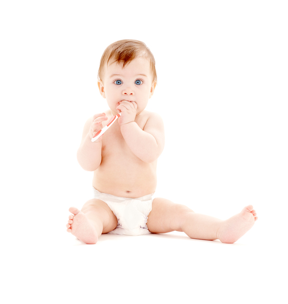 Ein kleines Kind in einer Windel sitzt aufrecht, mit einer Zahnbürste in der Hand, die es im Mund hat.