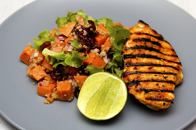 Gegrillte Hühnerbrust, gegrilltes Gemüse, auf einem weißen Teller.