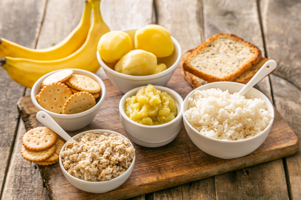 Beispiel für eine geeignete Ernährung bei akutem Durchfall - Reis, Kartoffeln, Bananen, Cracker, Kekse, in Schalen und auf einem Holzbrett.
