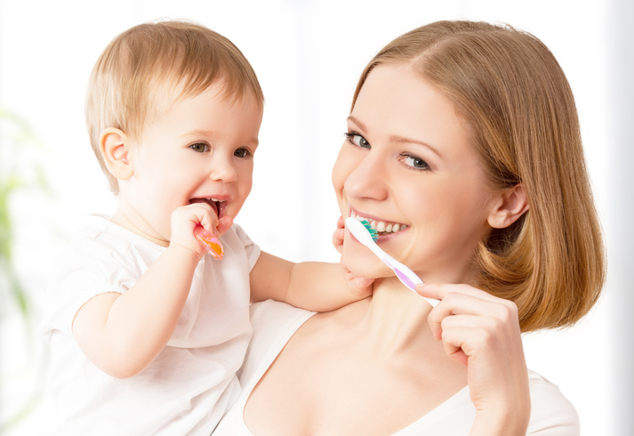 Eine Mutter putzt sich die Zähne mit ihrem Kind im Arm.