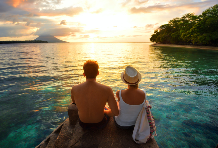 Paar sitzt bei Sonnenaufgang auf einem Felsen am Meer