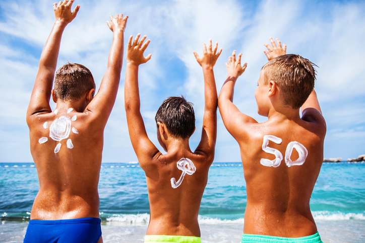 Sonnencreme für Kinder mit OF 50, Kinder sind am Strand am Meer und genießen sich, ihre Hände sind oben