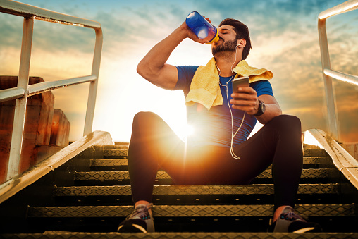 Ein Sportler, der auf der Treppe sitzt. Sonnenuntergang. Trinken eines Nahrungsergänzungsmittels aus einer Dose.