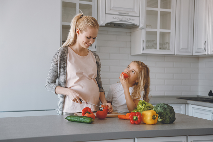 Schwangere Mutter und Tochter bereiten in der Küche eine gesunde Mahlzeit zu.