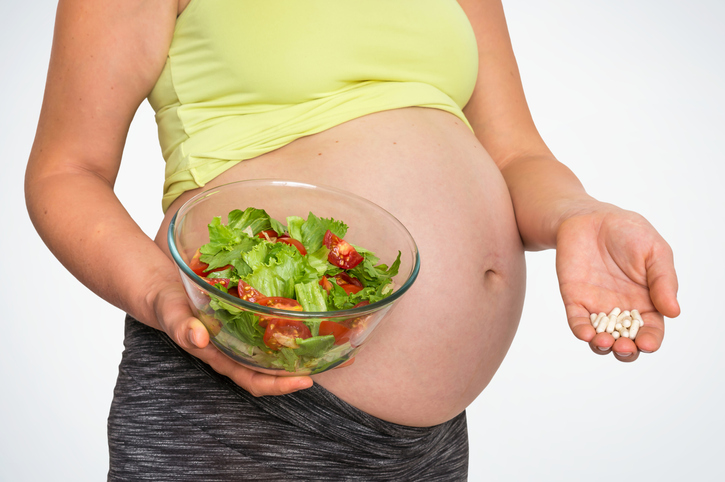 Schwangere Frau mit Salat und Pillen