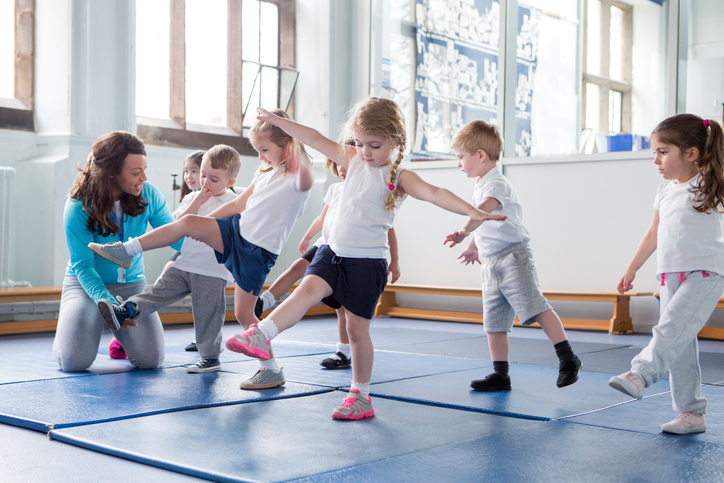 Kleine Kinder in der Turnhalle, die mit dem Lehrer üben.