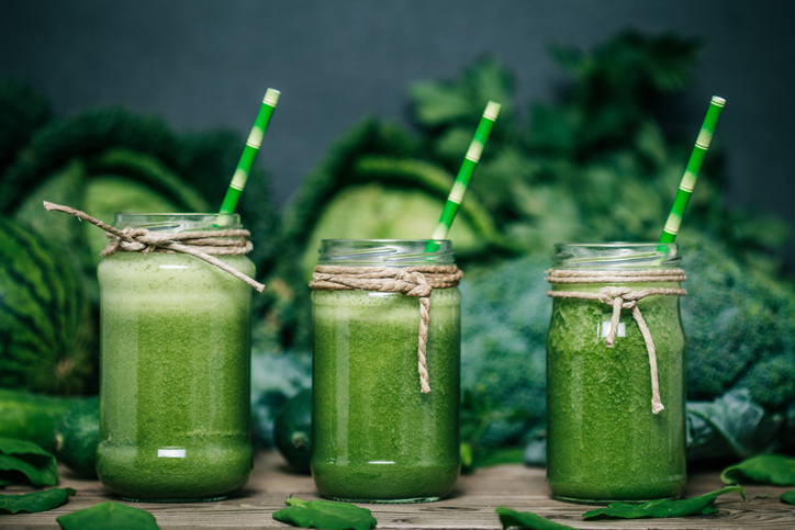 Grüner Gemüse-Smoothie, drei Gläser, im Hintergrund Kohl, Brokkoli und Erbsen