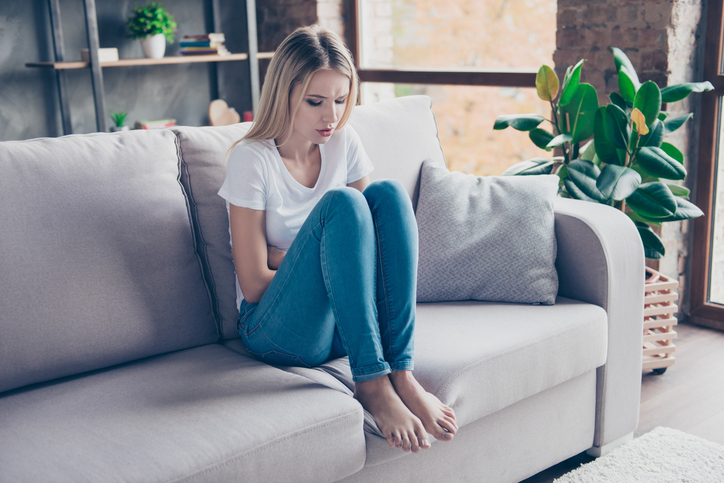 die Frau sitzt mit Schmerzen auf dem Sofa 