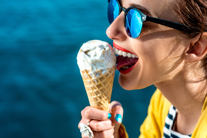 Frau mit Sonnenbrille schleckt Eis am Wasser