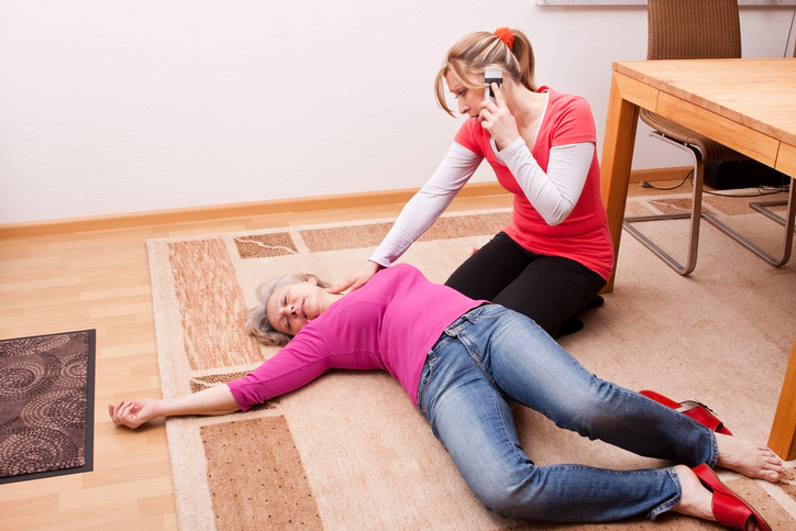 Die Frau liegt auf dem Boden und ist bewusstlos. Die andere Frau ruft telefonisch um Hilfe.