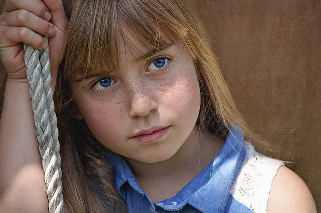 ein junges Mädchen, das auf einer Schaukel sitzt, mit neutralem Blick, blaue Augen