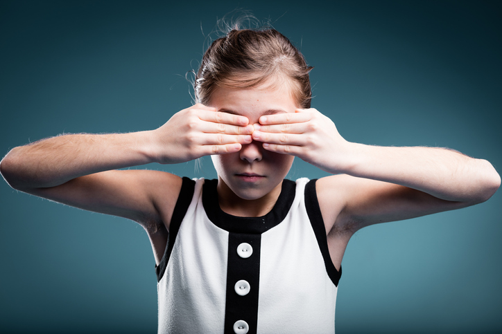 ein junges Mädchen bedeckt ihre Augen als Zeichen der Blindheit