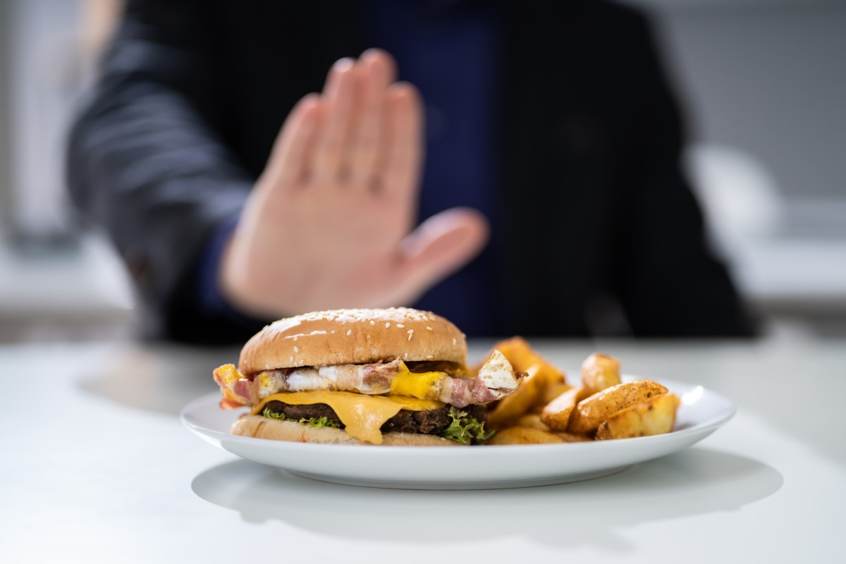 Ungeeignete Lebensmittel als Ursache für Sodbrennen - ein Hamburger auf einem Teller, den ein Mann ablehnt