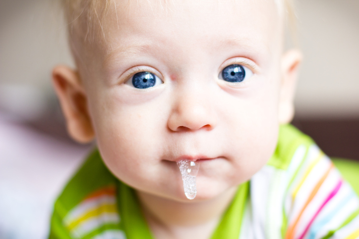 Ein kleines Kind, ein Säugling, sabbert, bekommt seinen ersten Zahn