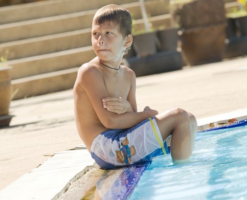 Der Junge sitzt am Pool, die Füße im Wasser, ihm ist kalt.