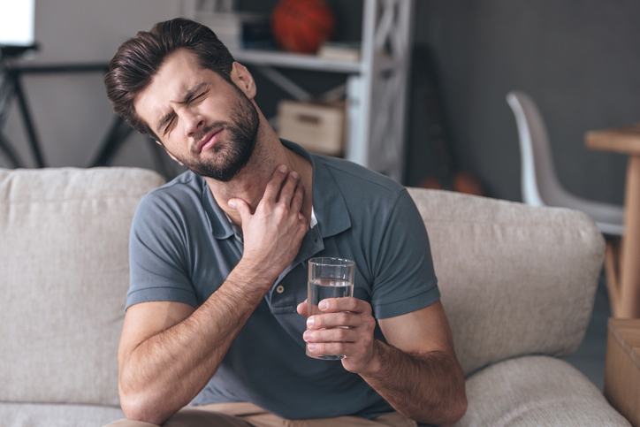 Ein Mann hat Halsschmerzen - er wird durch das Trinken von Wasser verschlimmert