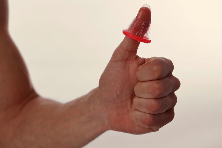 Ein Mann hält ein Kondom an seinem Finger (Daumen) als Symbol für den Schutz vor sexuell übertragbaren Krankheiten und vor der Befruchtung der Eizelle durch Spermien