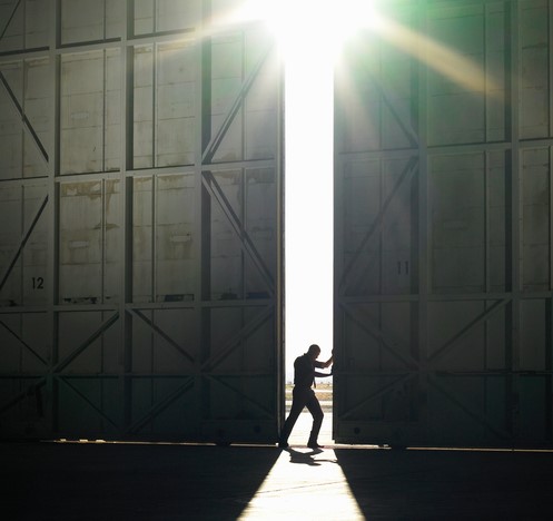 Ein Mann geht aus der dunklen Halle ins grelle Licht, die Sonne scheint, er öffnet eine Tür in der Halle