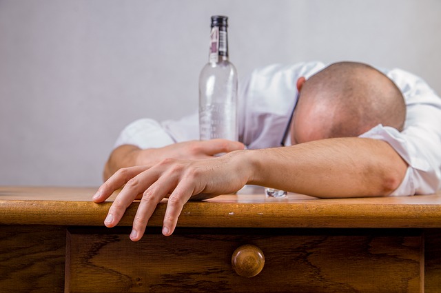 Alkoholismus ist die Ursache für Stimmungsstörungen, ein Mann liegt auf einem Tisch und hält eine leere Flasche Alkohol in der Hand, ein Alkoholiker