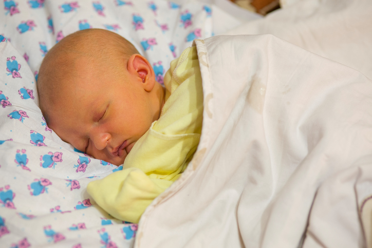 Neugeborenes, im Kinderbett liegend, angezogen, zugedeckt, Neugeborenengelbsucht, gelbliche Haut