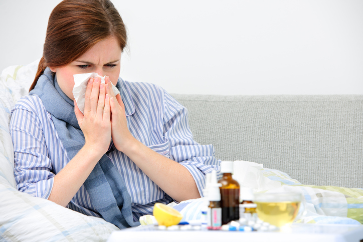Eine Frau putzt sich die Nase, wegen einer Erkältung, die die Ursache für verschiedene Beschwerden ist, im Bild sind Medikamente, Pillen, Flasche, Spray, Zitrone
