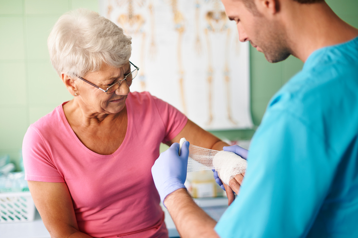 Eine Frau, eine Seniorin, hat eine Armverletzung und wird von einem Sanitäter behandelt.